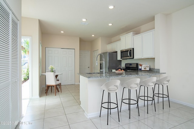 kitchen with a breakfast bar area, dark stone countertops, appliances with stainless steel finishes, kitchen peninsula, and white cabinets