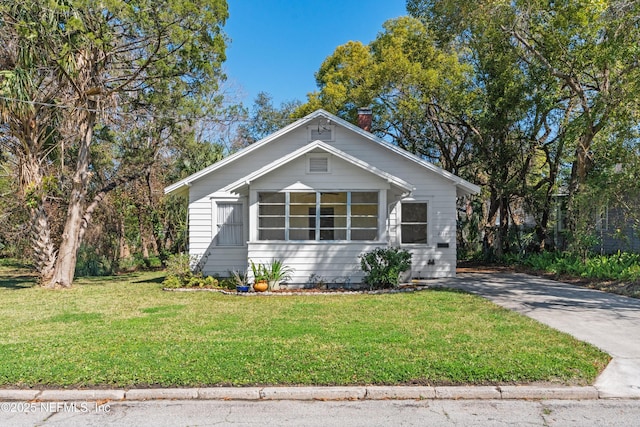 bungalow-style home with concrete driveway, a chimney, and a front yard