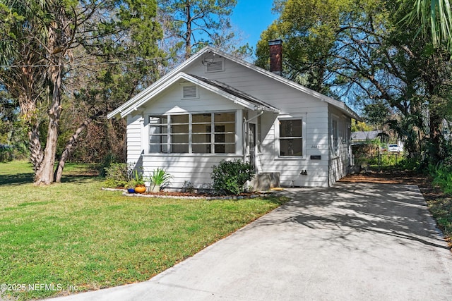 bungalow-style house with driveway, a front lawn, and a chimney