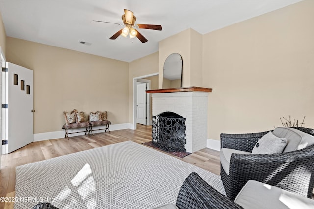 living room with a brick fireplace, light wood-style flooring, visible vents, and baseboards