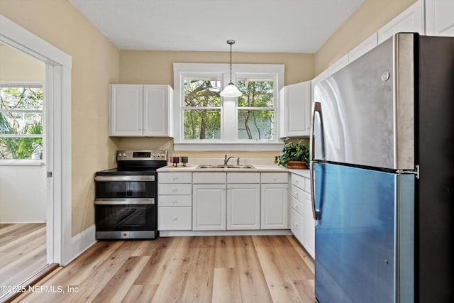 kitchen featuring stainless steel appliances, a sink, white cabinets, hanging light fixtures, and light countertops