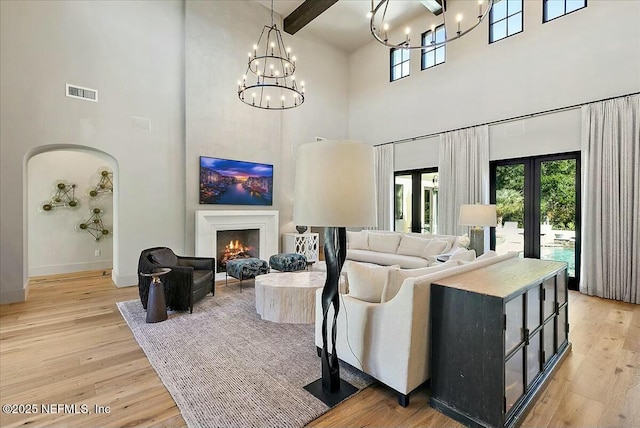 living room featuring beamed ceiling, a notable chandelier, light hardwood / wood-style floors, and french doors