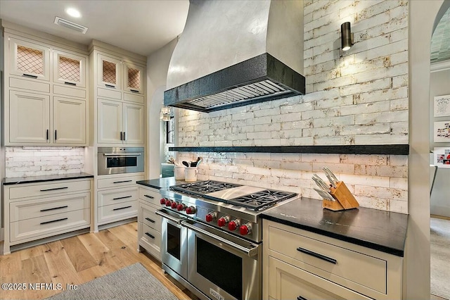 kitchen featuring light hardwood / wood-style floors, custom range hood, brick wall, and appliances with stainless steel finishes