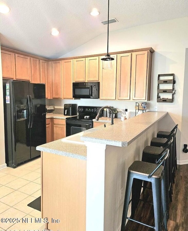 kitchen featuring pendant lighting, lofted ceiling, black appliances, a kitchen bar, and kitchen peninsula