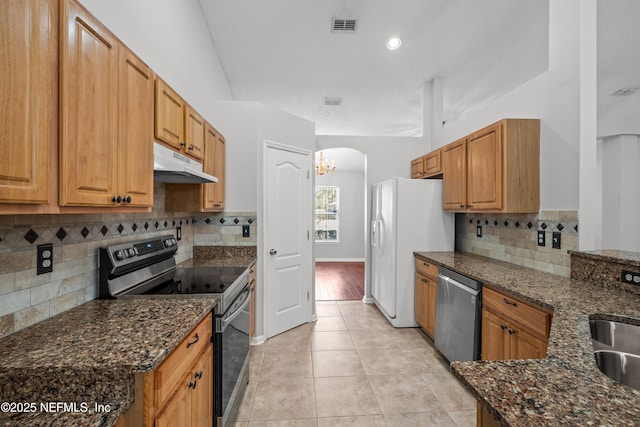 kitchen featuring sink, light tile patterned floors, dark stone countertops, stainless steel appliances, and backsplash