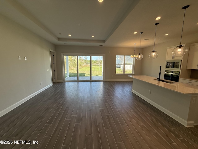 unfurnished living room with baseboards, a raised ceiling, dark wood finished floors, and recessed lighting