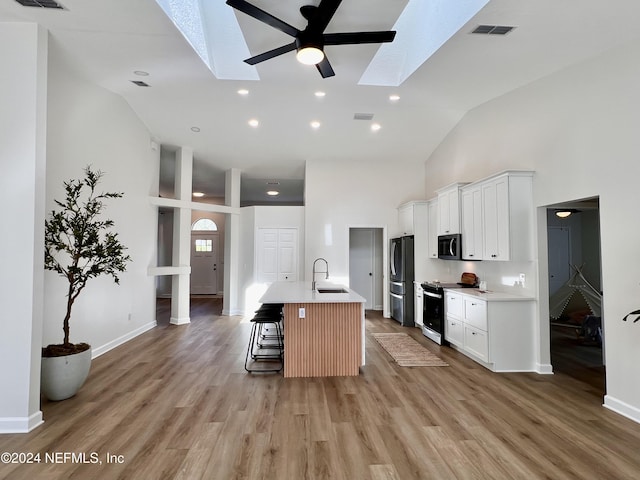 kitchen featuring sink, appliances with stainless steel finishes, white cabinetry, a skylight, and an island with sink