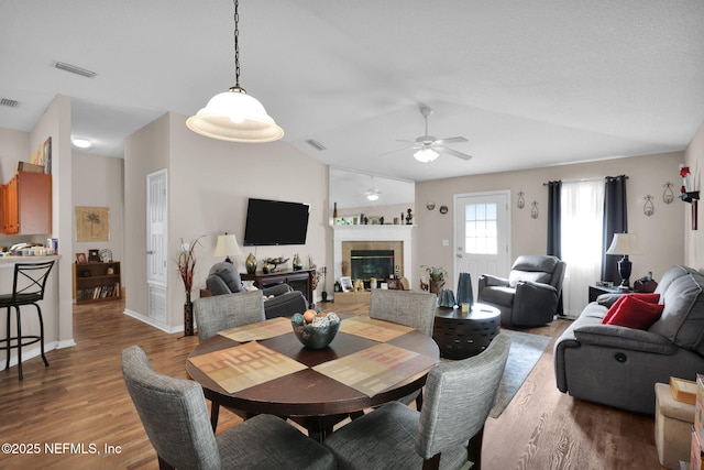 dining area with vaulted ceiling, a tiled fireplace, and hardwood / wood-style floors