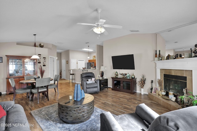 living room with lofted ceiling, a tiled fireplace, wood-type flooring, and ceiling fan