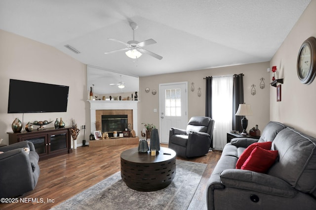 living room featuring hardwood / wood-style flooring, vaulted ceiling, a tile fireplace, and ceiling fan