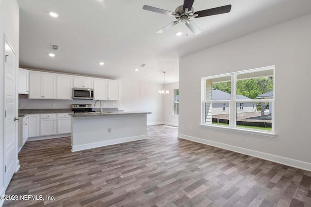 kitchen featuring dark wood-type flooring, decorative light fixtures, appliances with stainless steel finishes, a kitchen island with sink, and white cabinets