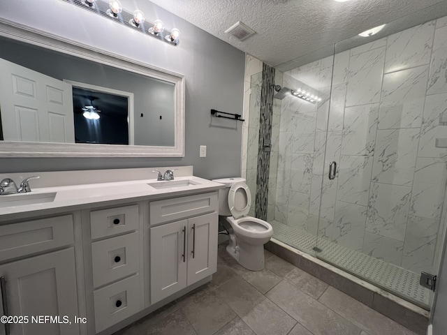 bathroom with a shower with shower door, vanity, ceiling fan, toilet, and a textured ceiling