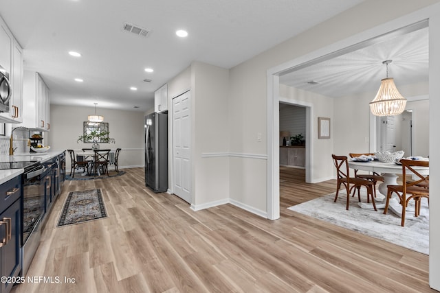 kitchen featuring stainless steel electric range oven, white cabinetry, hanging light fixtures, black fridge, and light hardwood / wood-style flooring