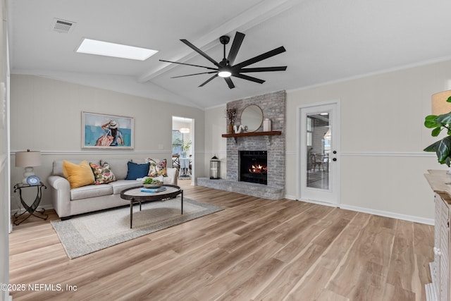 living room featuring crown molding, light hardwood / wood-style flooring, ceiling fan, lofted ceiling with beams, and a brick fireplace