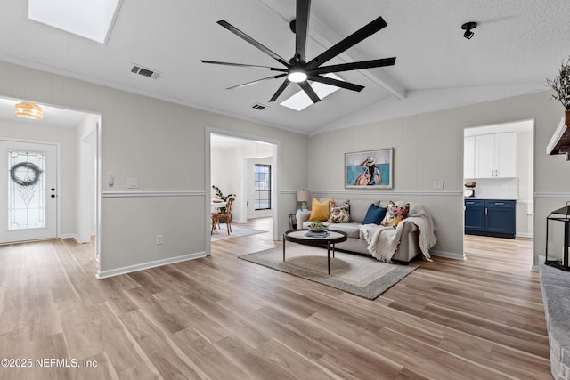 living room featuring ceiling fan, a textured ceiling, light hardwood / wood-style floors, and vaulted ceiling with skylight