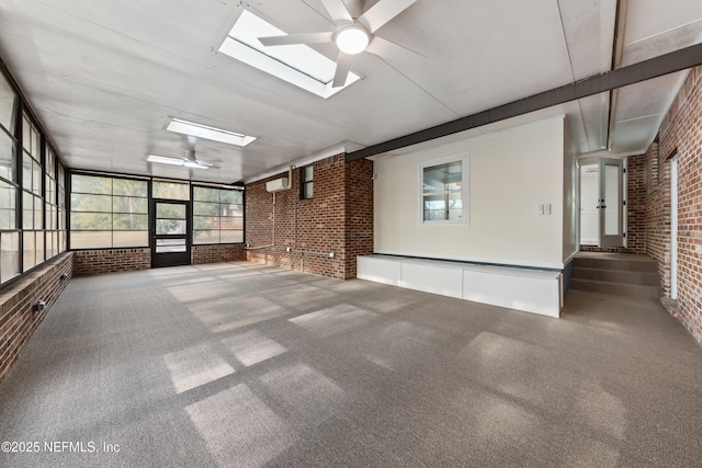 interior space featuring ceiling fan, brick wall, carpet flooring, and a skylight