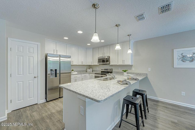 kitchen with stainless steel appliances, hanging light fixtures, white cabinets, and kitchen peninsula