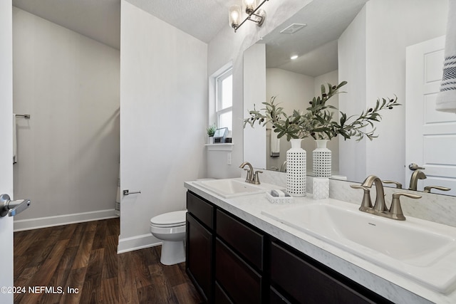 bathroom featuring wood-type flooring, toilet, vanity, and a textured ceiling