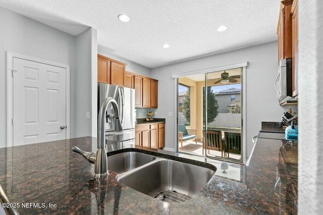 kitchen featuring appliances with stainless steel finishes, sink, dark stone countertops, and a textured ceiling