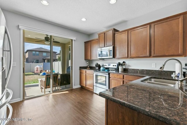 kitchen featuring sink, dark wood-type flooring, dark stone countertops, stainless steel appliances, and a textured ceiling