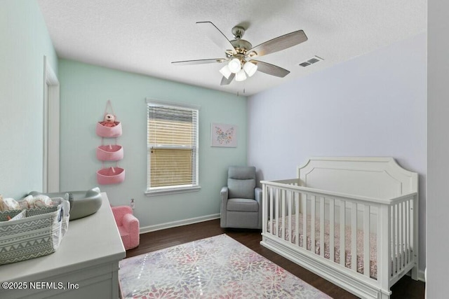 bedroom featuring dark wood-type flooring, a crib, and ceiling fan