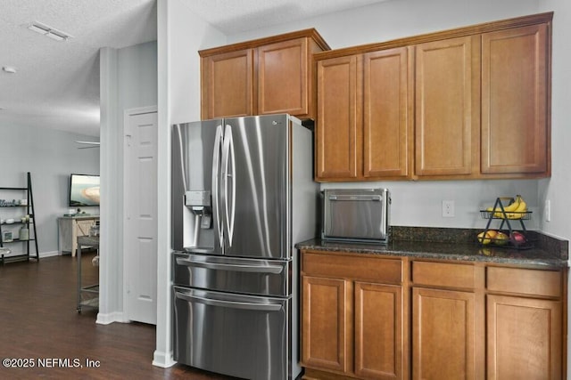 kitchen with dark stone countertops, stainless steel fridge with ice dispenser, dark wood-type flooring, and a textured ceiling