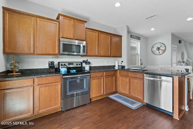 kitchen featuring appliances with stainless steel finishes, dark hardwood / wood-style flooring, kitchen peninsula, and sink