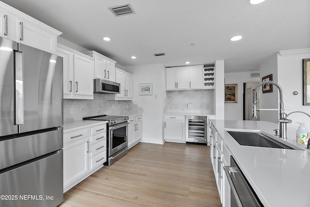 kitchen featuring sink, white cabinets, beverage cooler, stainless steel appliances, and light hardwood / wood-style flooring