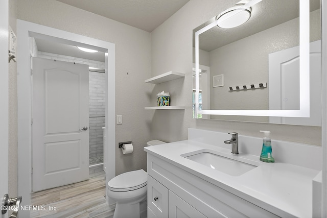 bathroom with hardwood / wood-style flooring, vanity, walk in shower, and toilet