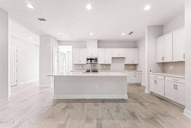 kitchen featuring white cabinetry, backsplash, a kitchen island with sink, and light hardwood / wood-style flooring