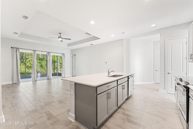 kitchen featuring gray cabinetry, sink, a tray ceiling, and an island with sink