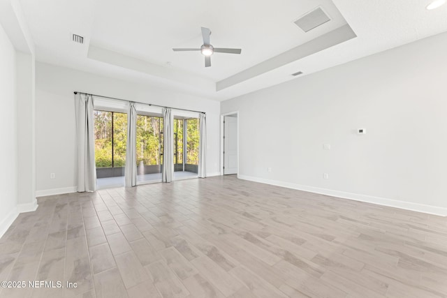 unfurnished room with a raised ceiling, ceiling fan, and light hardwood / wood-style flooring