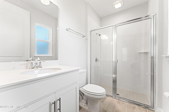 bathroom featuring toilet, wood-type flooring, vanity, and a shower with shower door