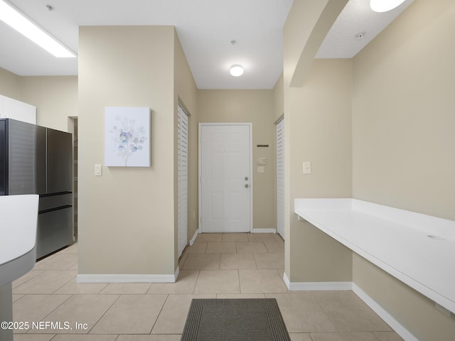 interior space with arched walkways, light tile patterned flooring, and baseboards