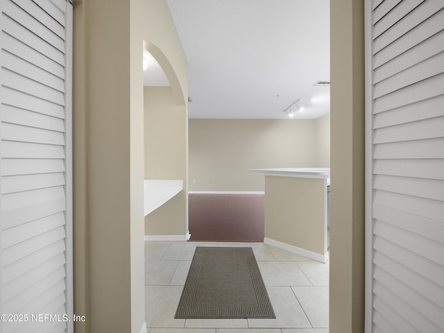 hall featuring arched walkways, visible vents, track lighting, tile patterned flooring, and baseboards