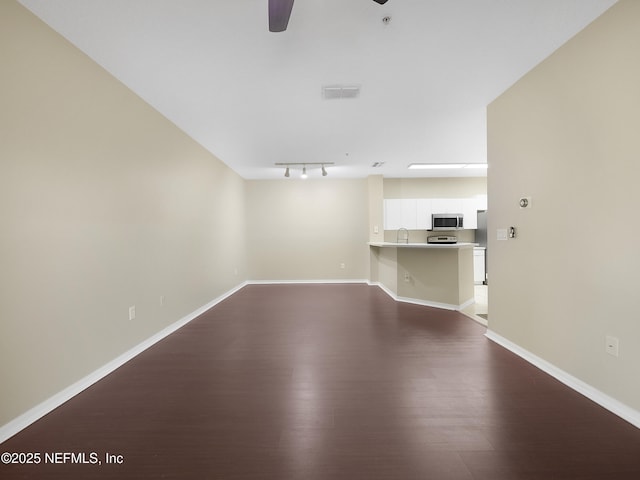 unfurnished living room featuring baseboards, track lighting, visible vents, and dark wood-type flooring