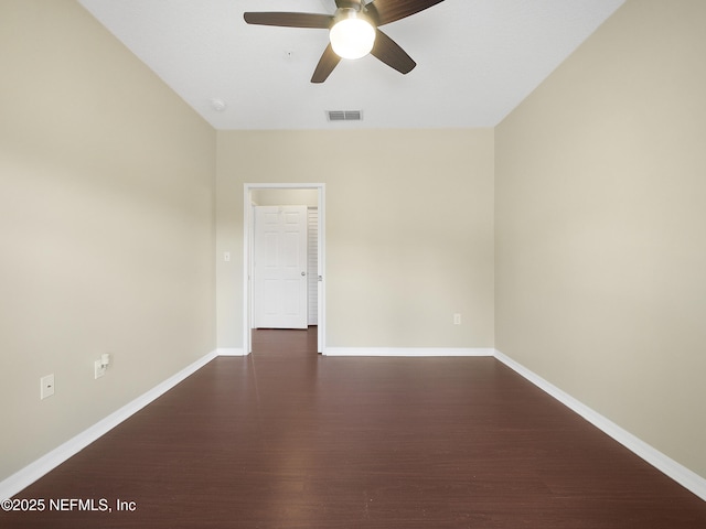 empty room with dark wood-style floors, a ceiling fan, visible vents, and baseboards