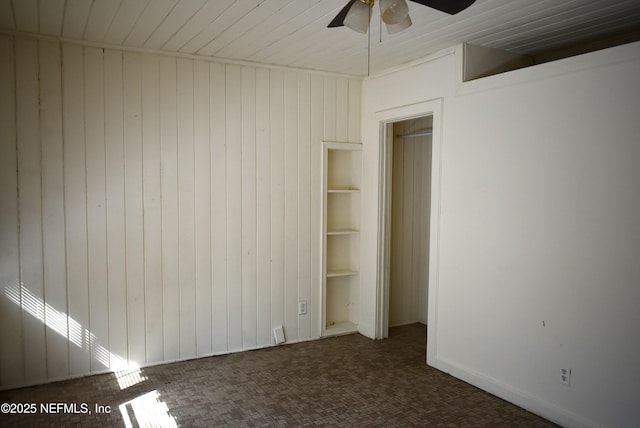 unfurnished bedroom with ceiling fan, dark carpet, and wood walls