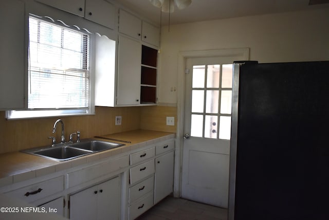 kitchen with sink, stainless steel fridge, tasteful backsplash, tile counters, and white cabinets