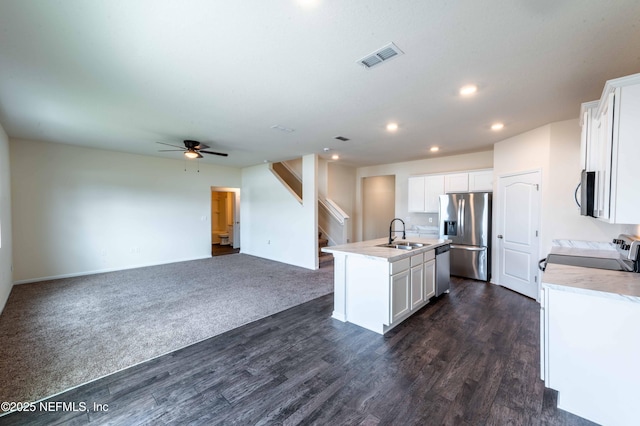 kitchen with an island with sink, sink, white cabinets, stainless steel appliances, and dark wood-type flooring