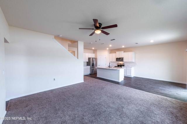 unfurnished living room featuring dark colored carpet, sink, and ceiling fan