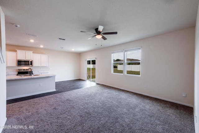 unfurnished living room with dark colored carpet, sink, and ceiling fan