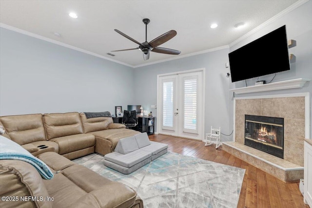 living room with crown molding, light hardwood / wood-style flooring, a tile fireplace, ceiling fan, and french doors