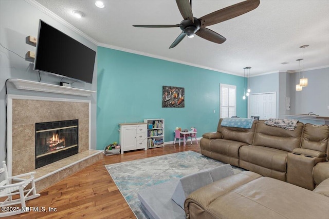 living room featuring a tiled fireplace, crown molding, a textured ceiling, and light wood-type flooring