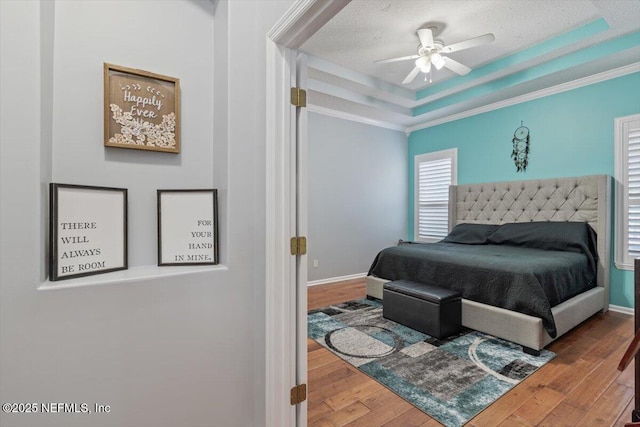 bedroom with wood-type flooring, a textured ceiling, ornamental molding, a tray ceiling, and ceiling fan