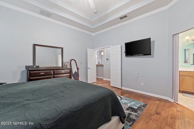 bedroom with connected bathroom, crown molding, light wood-type flooring, a raised ceiling, and ceiling fan