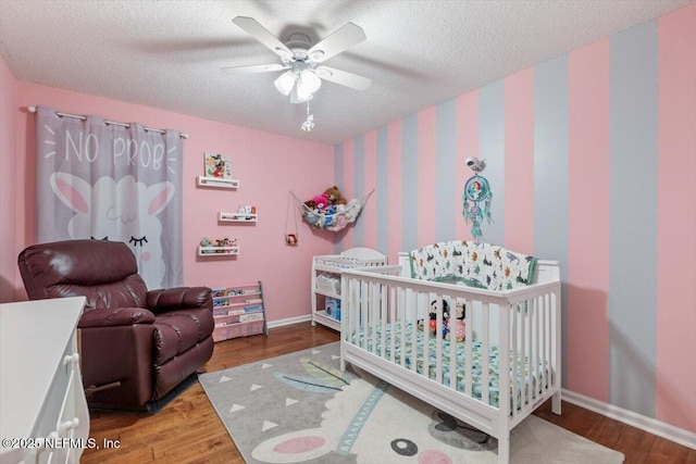 bedroom featuring ceiling fan, wood-type flooring, a textured ceiling, and a crib