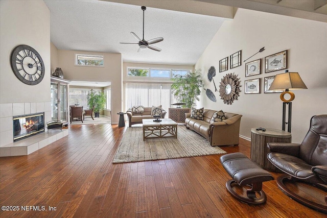 living room featuring high vaulted ceiling, a textured ceiling, hardwood / wood-style flooring, ceiling fan, and a fireplace