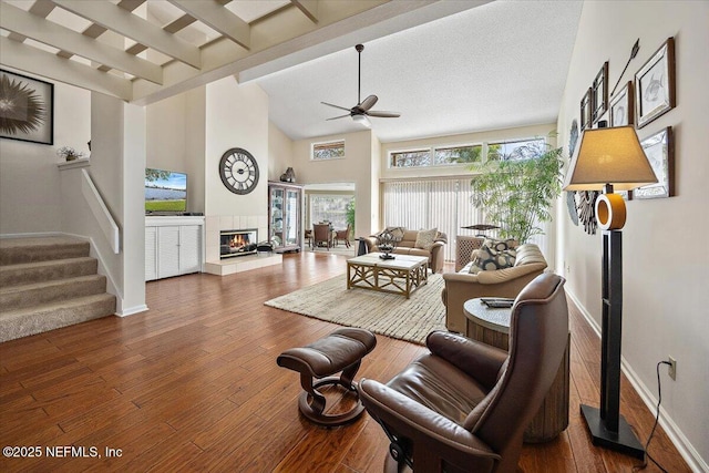 living room featuring high vaulted ceiling, beamed ceiling, dark hardwood / wood-style flooring, a tiled fireplace, and ceiling fan