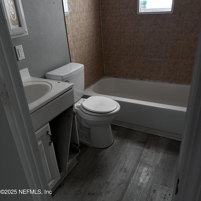 full bathroom featuring vanity, hardwood / wood-style flooring, tiled shower / bath combo, and toilet